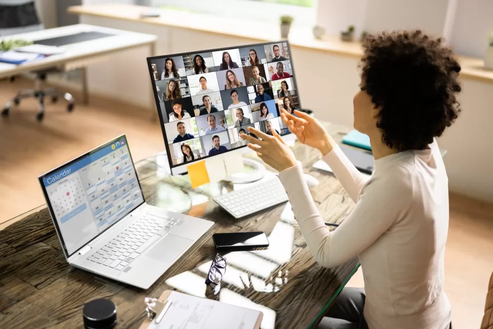 Woman at desk with laptop and extra monitor with Zoom session open.